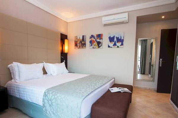 Hotelzimmer im Bianca Beach Resort mit Bett, Kissen, Spiegel und Kunstwerken an der Wand.