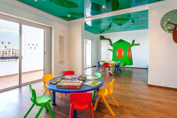 Kinderspielzimmer im Bianca Beach Resort mit bunten Tischen und Stühlen, blauem Tisch, grüner Wandmalerei und bemalter Decke.