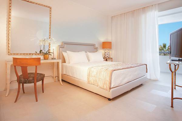 Schlafzimmer im Grecotel Creta Palace mit Bett, Tisch, Stuhl und Spiegel.