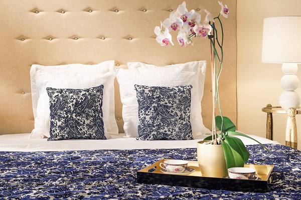 Bett im Grecotel Creta Palast mit blauem Bettwäsche und Kissen, Orchideen, und Tassen auf einem Tablett.
