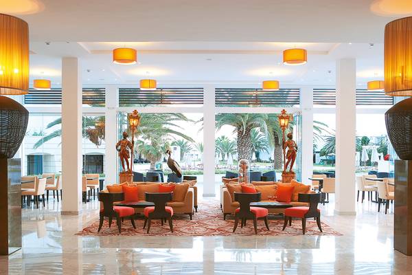 Hotellobby des Grecotel Creta Palace mit braunen Sofas, roten Kissen, Tisch und Stühlen.