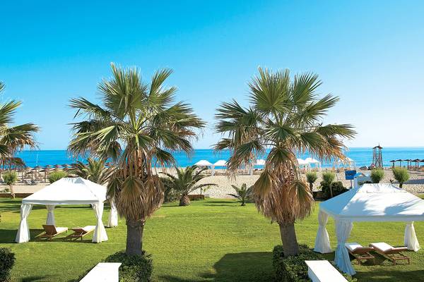 Außenbereich des Grecotel Creta Palace Hotels mit weißen Zelten und Palmen vor einem Strand