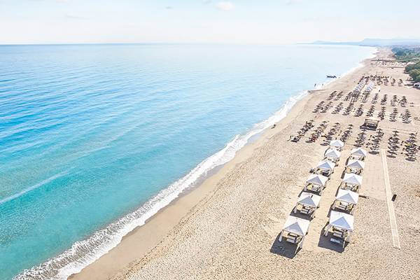 Luftaufnahme des Strandes am Grecotel Creta Palace Hotel mit vielen Sonnenschirmen und blauem Meer