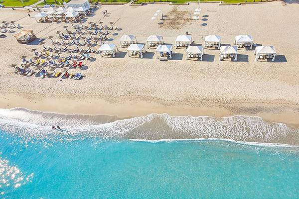 Luftaufnahme eines griechischen Strandes mit weißen Sonnenschirmen und Liegen am Grecotel Creta Palace