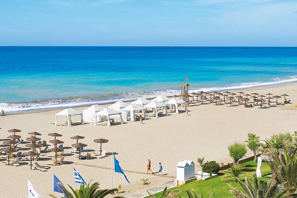 Luftaufnahme des Grecotel Creta Palace Strands mit weißen Sonnenschirmen und Liegestühlen.
