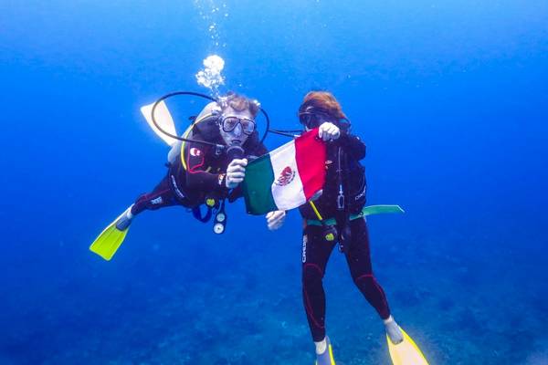 Zwei Taucher im Wasser halten eine mexikanische Flagge vor sich