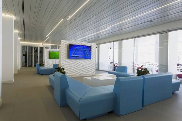 Lobby-Lounge-Bereich des Caserio Hotels mit blauen Sofas, Tischen und Fernsehern.