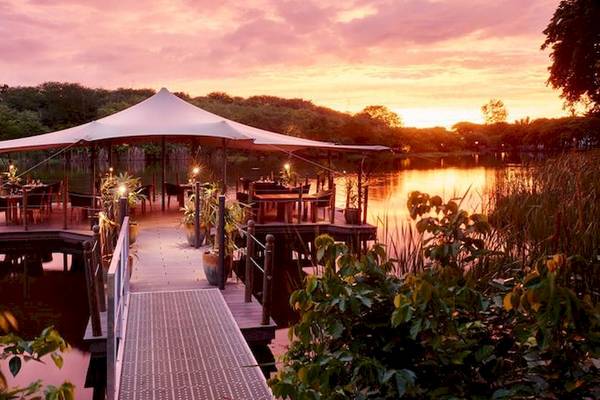 Außenbereich des Ravenala Attitude Hotels mit Pavillon und Tischen am See bei Sonnenuntergang