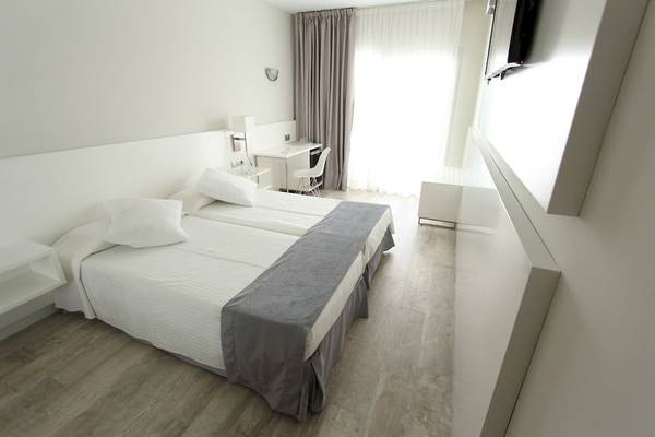 Das Schlafzimmer im Caserio Hotel mit zwei weißen Betten, grauen Decken und einem weißen Schreibtisch.