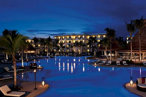 Nachtansicht des Swimmingpools des Secrets Akumal Riviera Maya Hotels, beleuchtet und voll mit Sonnenliegen.