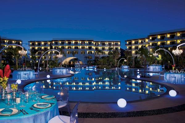 Der beleuchtete Swimmingpool des Secrets Akumal Riviera Maya Hotels bei Nacht mit runden Tischen und Stühlen.