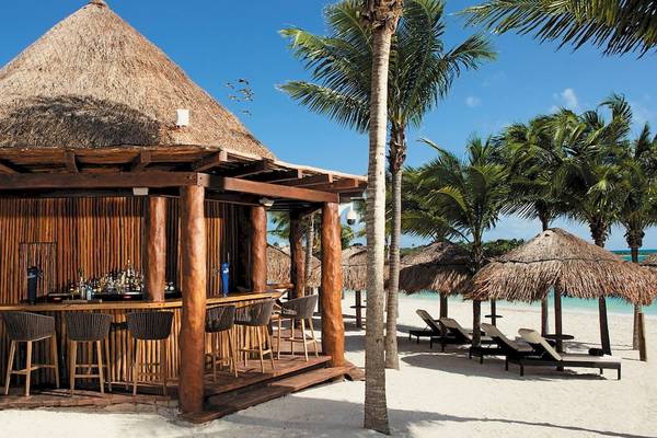 Bar in einer Hütte am Strand von Secrets Akumal Riviera Maya mit Stühlen und Tischen im Freien.