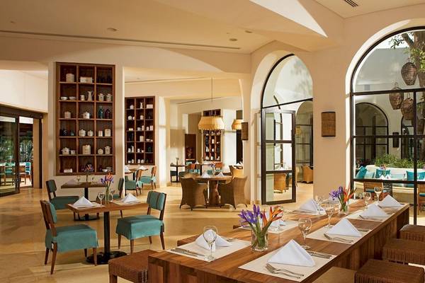 Innenansicht des Restaurants im Secrets Akumal Riviera Maya mit Holztischen, Stühlen und Tischdekoration.