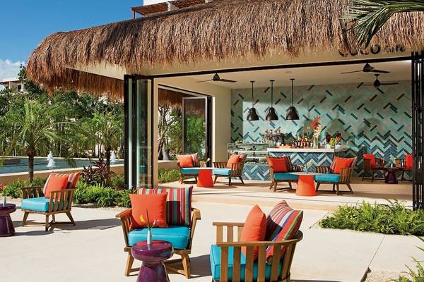 Lounge Bereich im Secrets Akumal Riviera Maya Hotel mit bunten Stühlen und Tischen, umgeben von tropischer Vegetation.