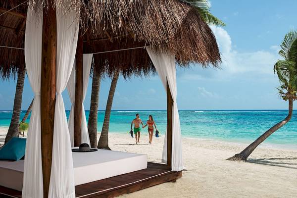 Strandpaar mit einem weißen Bett unter einer Strohhütte am Secrets Akumal Riviera Maya