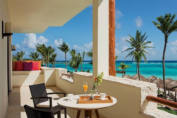 Balkonblick auf das Meer im Secrets Akumal Riviera Maya Hotel mit Tisch, Getränken und Sonnenliegen.