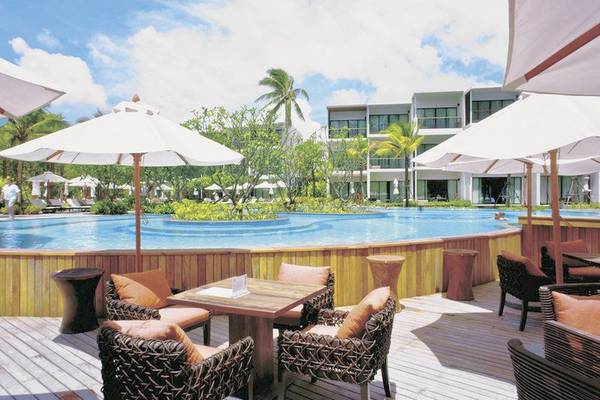 Pool-Terrasse im Holiday Inn Mai Khao Resort mit Sonnenschirmen und Tischen.