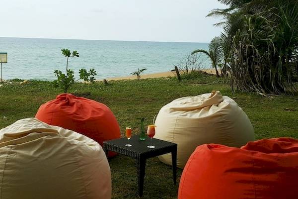 Strand mit drei roten und einem weissen Beanbag vor einem Tisch mit zwei Gläsern auf dem Holiday Inn Mai Khao Resort