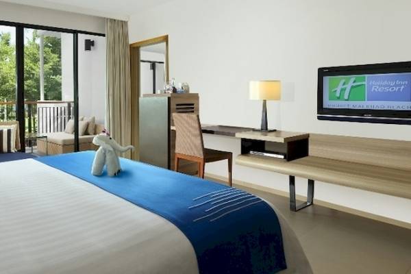 Hotelzimmer im Holiday Inn Mai Khao Resort mit einem großen Bett, Fernseher und Balkon.