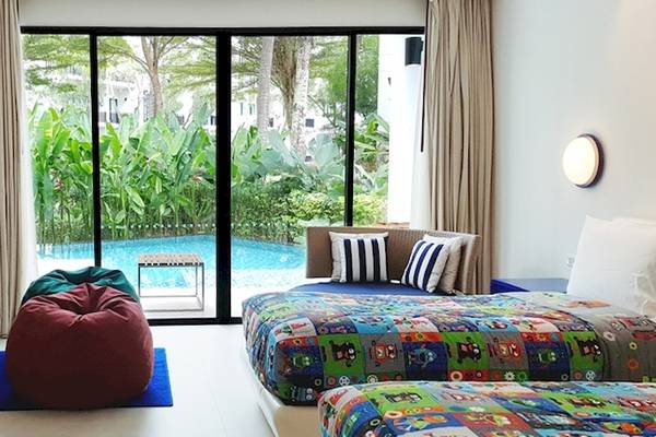 Zweibettzimmer im Holiday Inn Mai Khao Resort mit Panoramafenstern, Blick auf den Pool, Fernseher und gemütlichen Betten.
