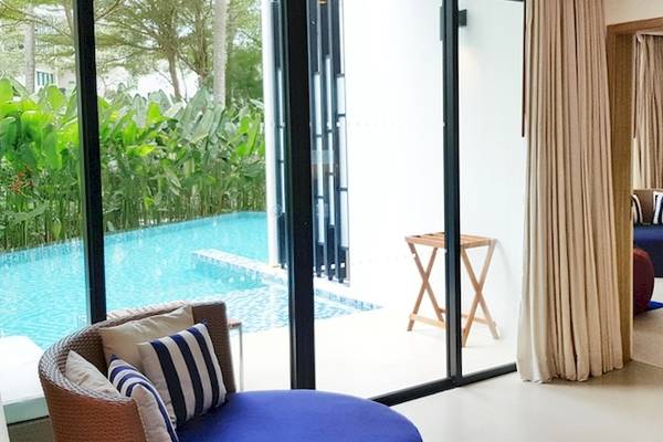 Ein modernes Zimmer mit Poolblick im Holiday Inn Mai Khao Resort, inklusive Sitzbereich und offenem Glasfenster.