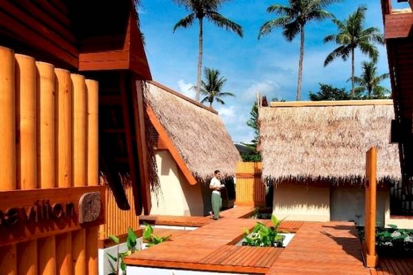 Außenbereich des Holiday Inn Mai Khao Resorts mit einem Mann, der auf einem Holzdeck steht, umgeben von tropischen Häusern und Palmen.