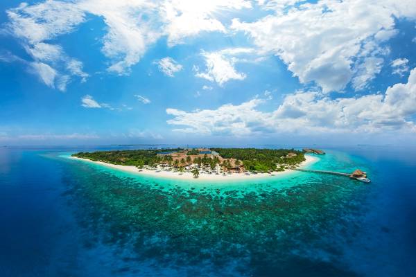 Luftaufnahme des Reethi Faru Resorts auf einer kleinen Insel mit einem Steg, Gebäuden und türkisfarbenem Wasser.