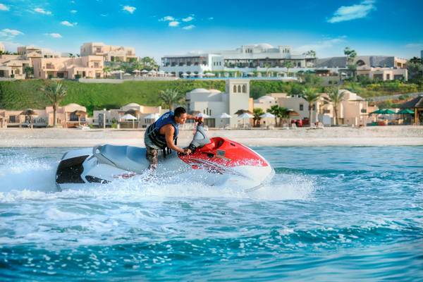 Ein Mann fährt einen Jetski vor den Gebäuden des Cove Rotana Resorts.