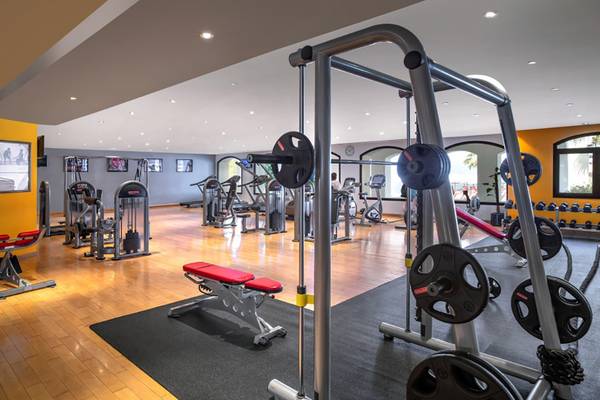 Fitnesscenter im Cove Rotana Resort mit verschiedenen Trainingsgeräten und einer Person, die eine Hantelbank benutzt.