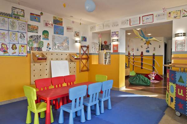 Kinderzimmer im Cove Rotana Resort mit bunten Stühlen, rotem Tisch und dekorierten Wänden.