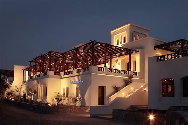 Außenansicht des The Cove Rotana Resort bei Nacht mit beleuchteter Terrasse und Gebäudebeleuchtung.