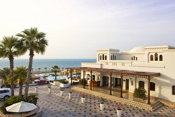 Außenansicht des Cove Rotana Resort Hotels mit Meerblick und gepflastertem Bereich.