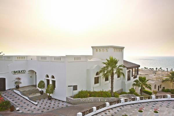 Außenansicht des The Cove Rotana Resort mit weißem Gebäude, Meer im Hintergrund und Basilico Restaurant.