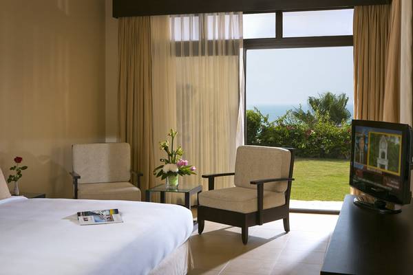 Hotelzimmer mit Meerblick und Fernseher, zwei Sessel und eine Tisch mit Blumen.