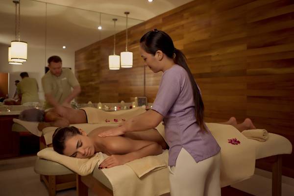 Eine Frau, die eine Massage im Hotel-Spa gibt, während ein Mann im Hintergrund arbeitet.