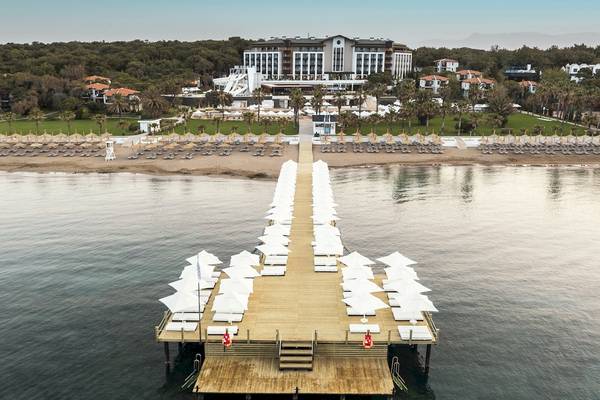 Luftaufnahme des Voyage Sorgun Hotels am Strand mit vielen Sonnenschirmen und Liegen.