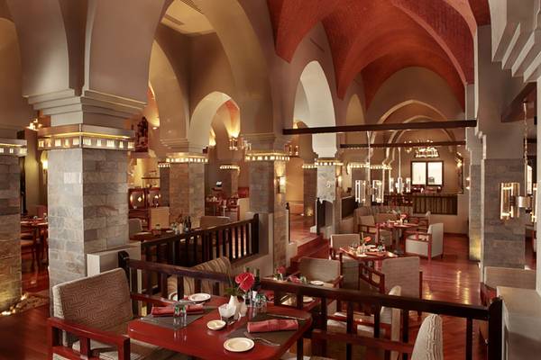Innenbereich des Restaurants The Cove Rotana Resort mit Holzboden, Steinwänden und bogenförmigen Strukturen.