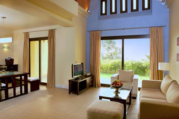Das Wohnzimmer des Cove Rotana Resort mit Fernseher, Esstisch und großem Fenster.