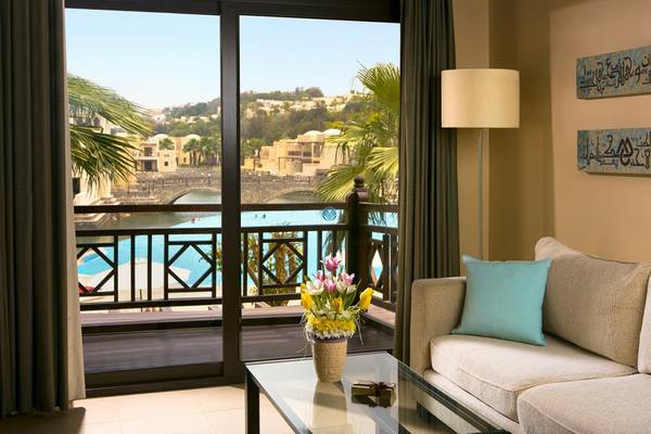 Blick vom Balkon des Cove Rotana Resorts auf einen Swimmingpool und eine Stadtlandschaft.