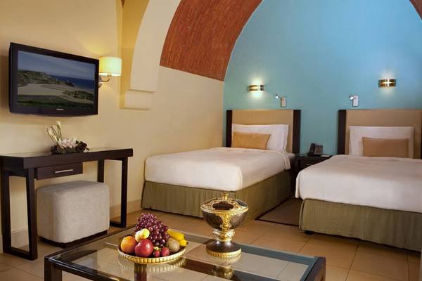 Hotelzimmer im Cove Rotana Resort mit zwei Betten, Fernseher und Früchten auf dem Tisch.