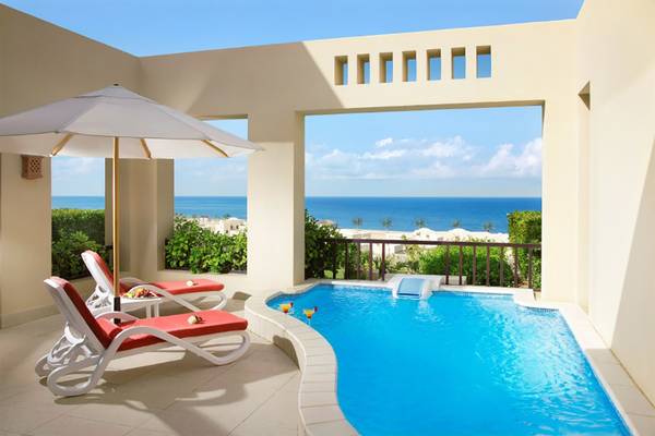 Balkon des Cove Rotana Resorts mit Swimmingpool und Meerblick, zwei Liegen und einem Schirm.
