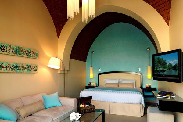 Schlafzimmer im Cove Rotana Resort mit Bett, Sofa, Tisch, Fernseher und dekorativen Elementen.