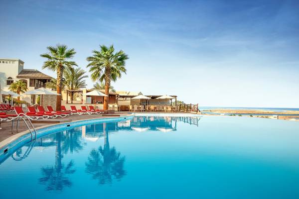 Außenpool des Cove Rotana Resort mit roten Sonnenliegen und Palmen im Vordergrund.