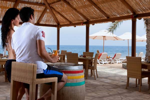 Paar am Strand des Cove Rotana Resorts mit Blick auf das Meer und Sonnenschirmen.