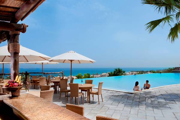 Hotelpool-Terrasse mit Meerblick im Cove Rotana Resort mit Personen und Sonnenschirmen.