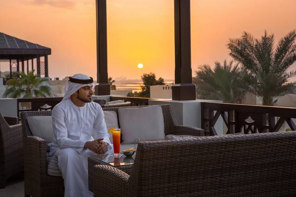 Ein Mann sitzt auf dem Balkon des Cove Rotana Resorts bei Sonnenuntergang.