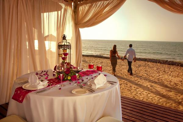 Das Cove Rotana Resort mit einem romantischen Essenstisch am Strand mit Blick auf das Meer.