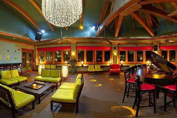 Loungebereich im Couples Negril Hotel mit grünen Sofas, einer Klavierbar und Deckenventilatoren.