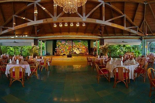 Innenbereich des Restaurants im Couples Negril Hotel mit Tisch und Stühlen, Bühne und Lampe.