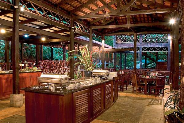 Innenansicht des Restaurants im Punta Leona Hotel mit Holzmöbeln und grüner Umgebung.